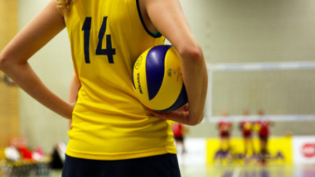 Rücken einer Volleyballspielerin in gelbem Trickot mit Volleyball unter ihrem Arm