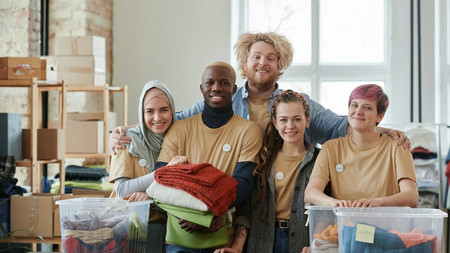 Gruppe engagierter Menschen mit Spenden in Kisten auf einem Tisch. Sie lächeln in die Kamera