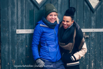 Zwei junge Frauen angelehnt an einer grünen Wand.