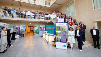Gruppenfoto aller Ausgezeichneten auf einer Treppe in einem Foyer, in dem Infostände aufgebaut wurden