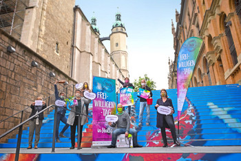 Mitarbeitende der Freiwilligen-Agentur auf der Treppe am hallenser Hallmarkt mit Plakaten zum Freiwilligentag